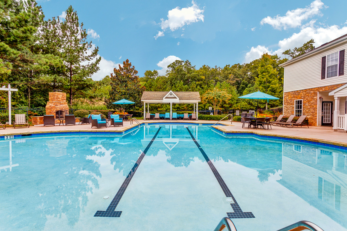 Inviting outdoor pool at Summer Park Apartments with sun loungers, cozy seating, and vibrant umbrellas set against lush greenery.