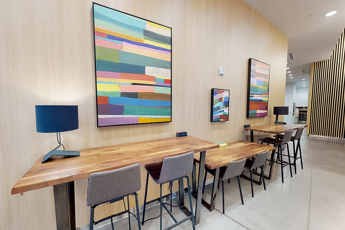 Modern workspace with sleek wooden tables, stylish chairs, and vibrant abstract art on walls, perfect for a creative atmosphere at Apt CoWork at Sugarmont Apartments in Salt Lake City