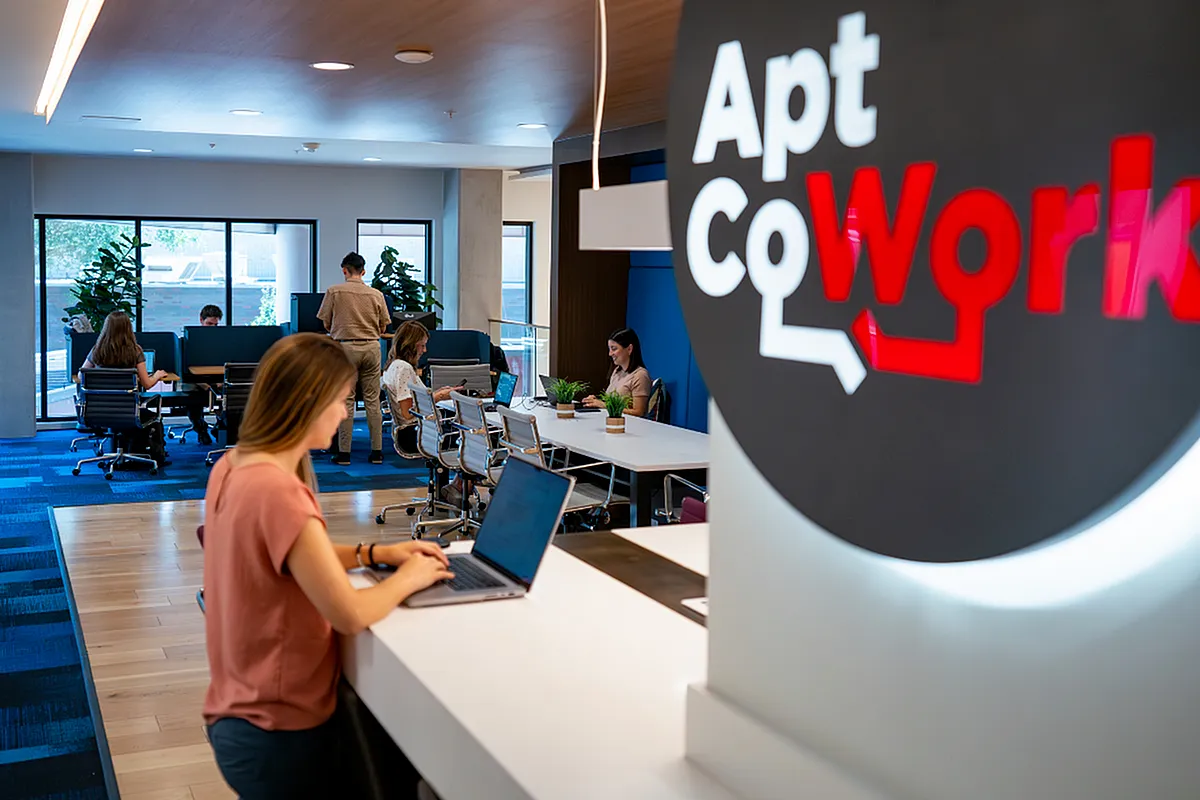 Modern coworking space with vibrant blue accents, featuring professionals working at communal desks under ample natural light at Apt CoWork at Sugarmont Apartments in Salt Lake City