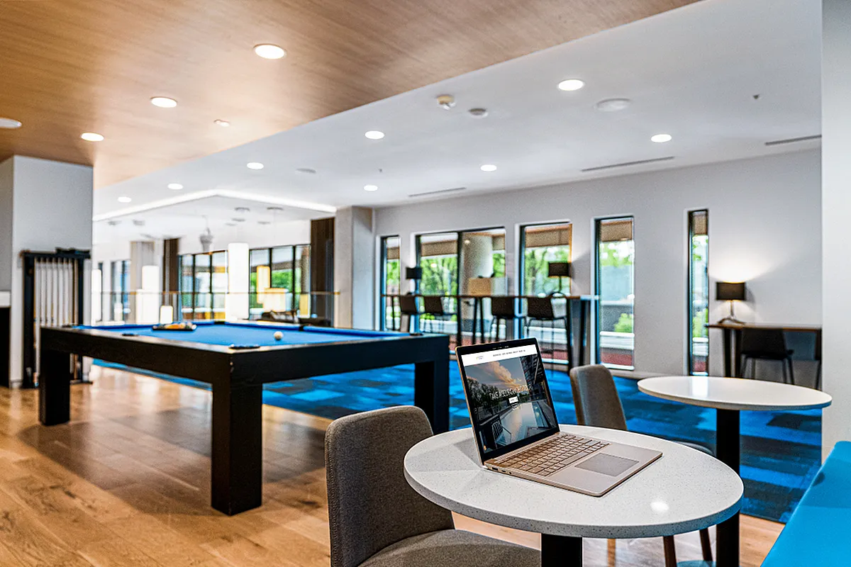 Modern apartment common area with a sleek pool table, stylish seating, and large windows offering abundant natural light  at Apt CoWork at Sugarmont Apartments in Sugarhouse