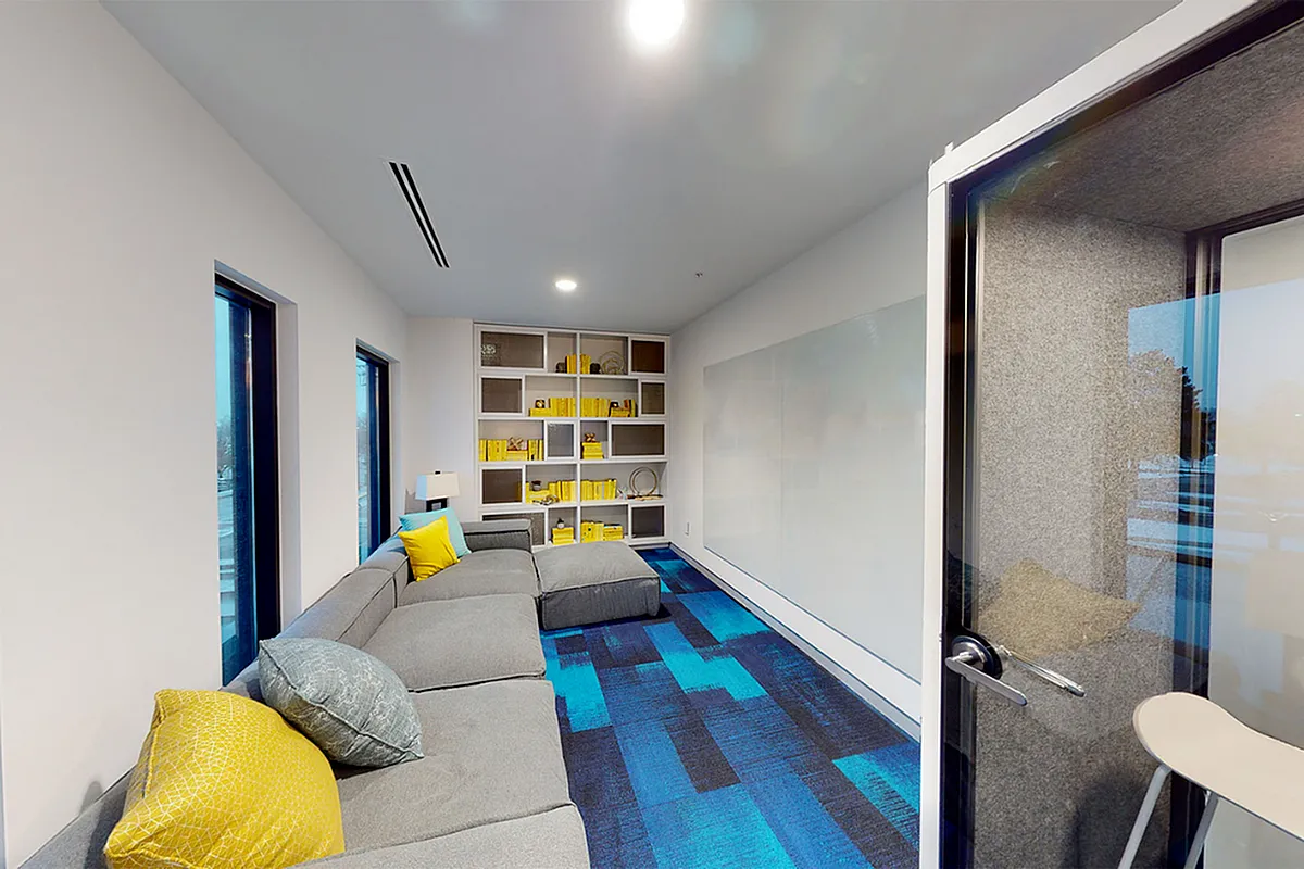 Modern apartment lounge with cozy gray sectional, vibrant yellow and blue accents, and chic built-in bookshelves  at Apt CoWork at Sugarmont Apartments in Sugar House