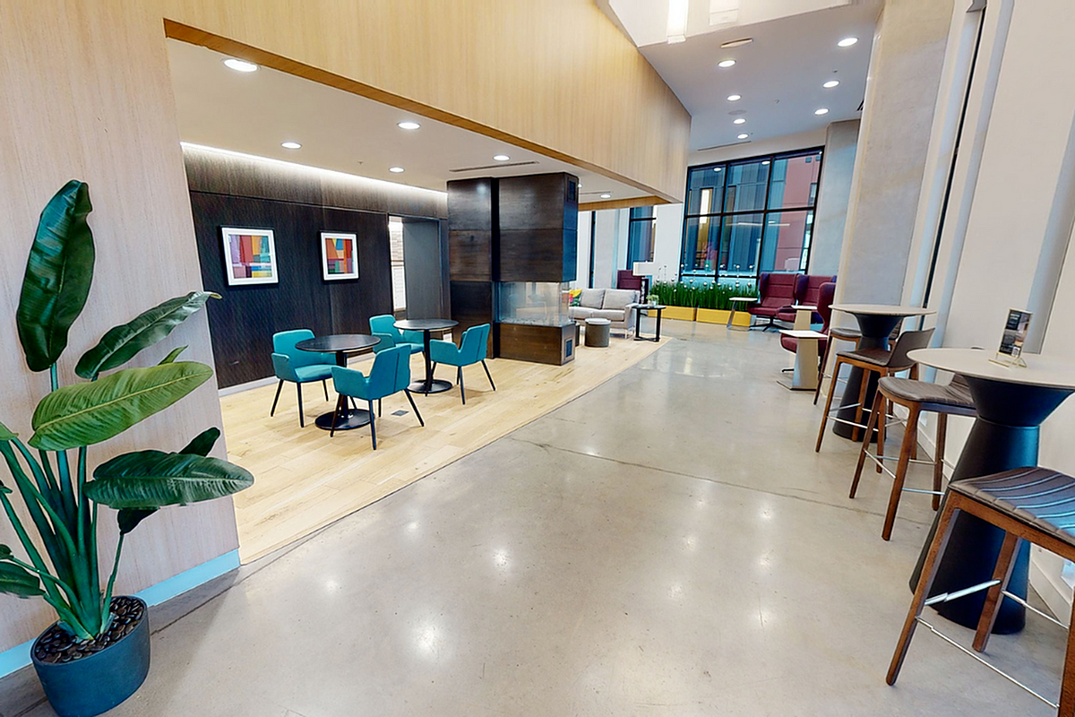 Modern communal lounge featuring stylish turquoise chairs, chic tables, and vibrant greenery in a spacious, well-lit setting  at Apt CoWork at Sugarmont Apartments in Sugar House