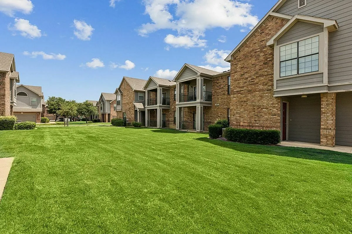 Charming suburban apartment complex with well-maintained lawns, elegant brick facades, and inviting balconies under a bright blue sky at Enclave on Golden Triangle in Fort Worth TX