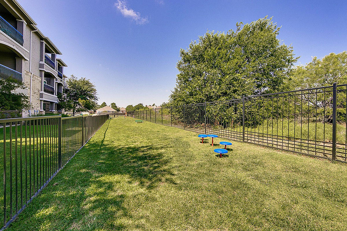 Spacious landscaped dog park with modern apartment building and secure fencing, perfect for pet-friendly outdoor enjoyment at Toscana at Valley Ridge Apartments.