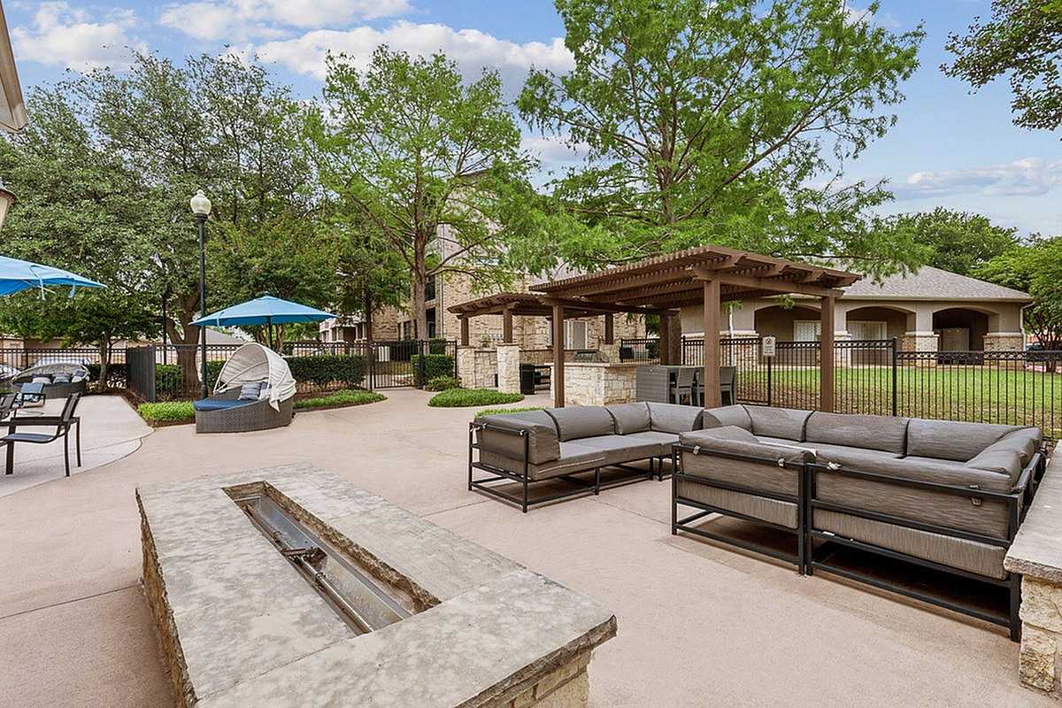 Inviting outdoor lounge with modern seating, shaded pergola, and lush green surroundings, perfect for relaxing and entertaining at Toscana at Valley Ridge Apartments.