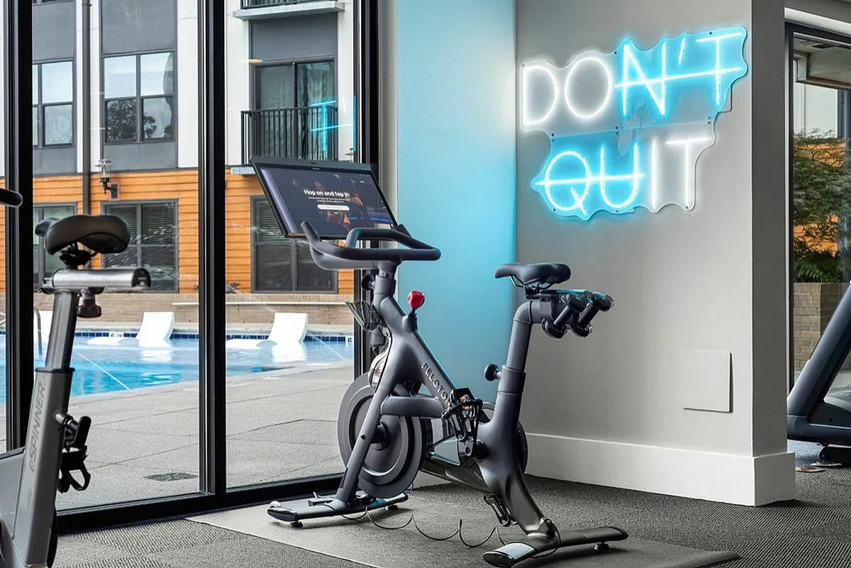 Modern apartment gym with state-of-the-art exercise bikes overlooking a sparkling pool and motivational neon sign, 'Don't Quit' at Cottonwood Westside Apartments in Midtown Atlanta