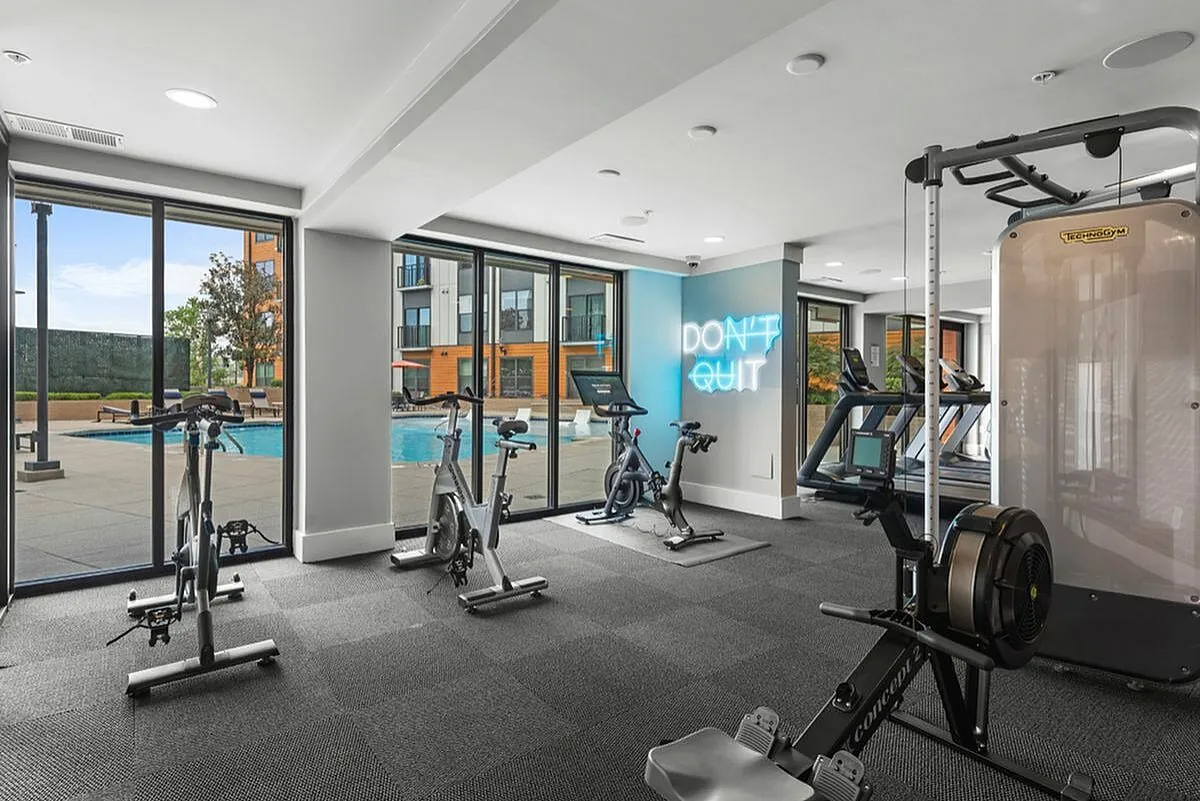 Modern fitness center with bright natural light, exercise equipment, and pool view, featuring a motivational 'Don't Quit' neon sign at Cottonwood Westside Apartments in Midtown Atlanta