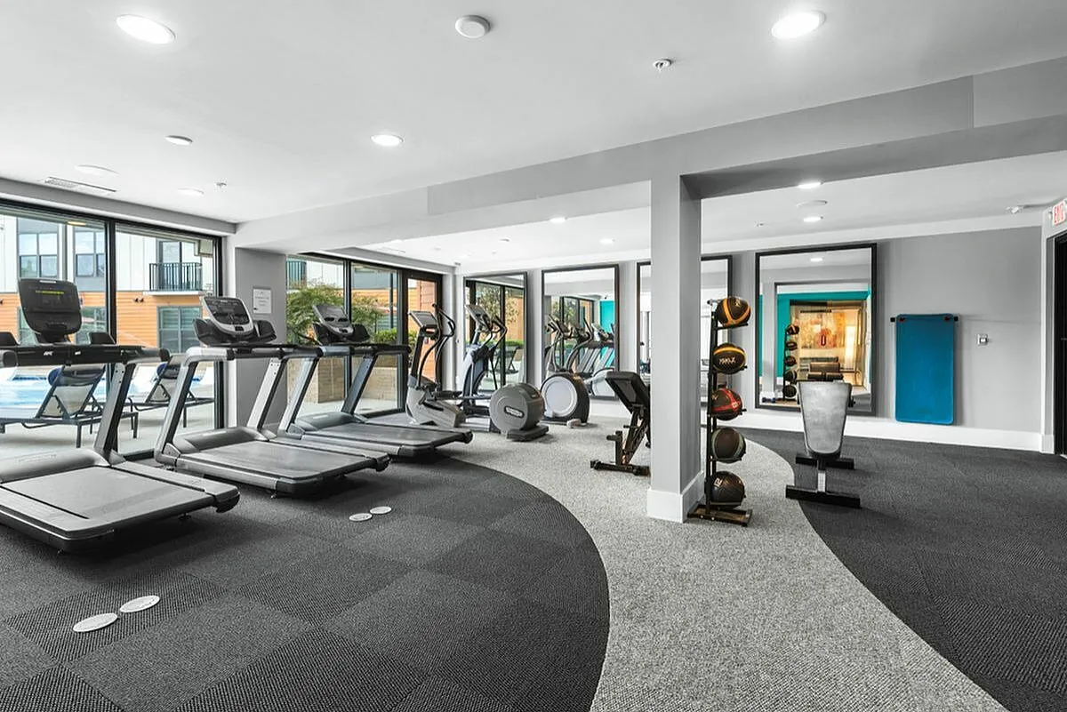 Modern fitness center with state-of-the-art gym equipment, including treadmills and exercise bikes, overlooking a pool through large windows at Cottonwood Westside Apartments in Midtown Atlanta