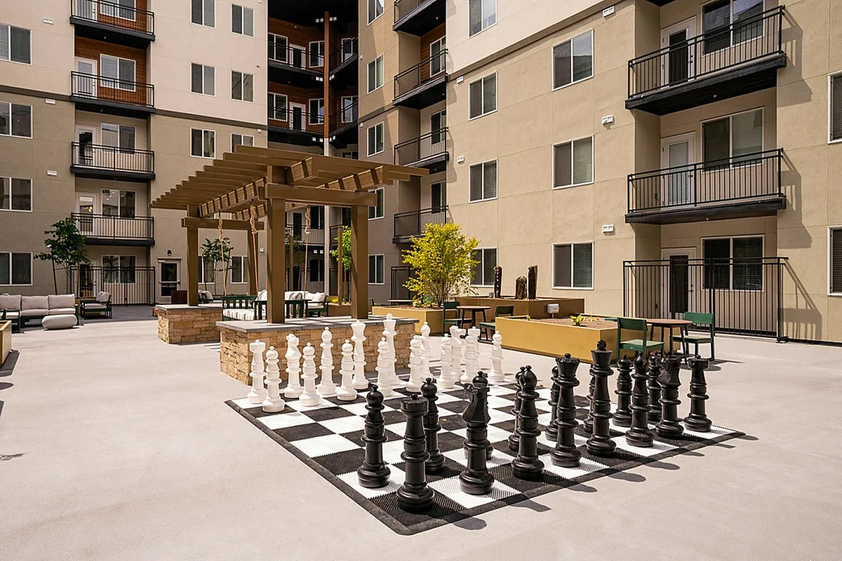 Modern apartment courtyard featuring a giant chess set, elegant seating areas, and lush greenery under a stylish pergola at Current Apartments.