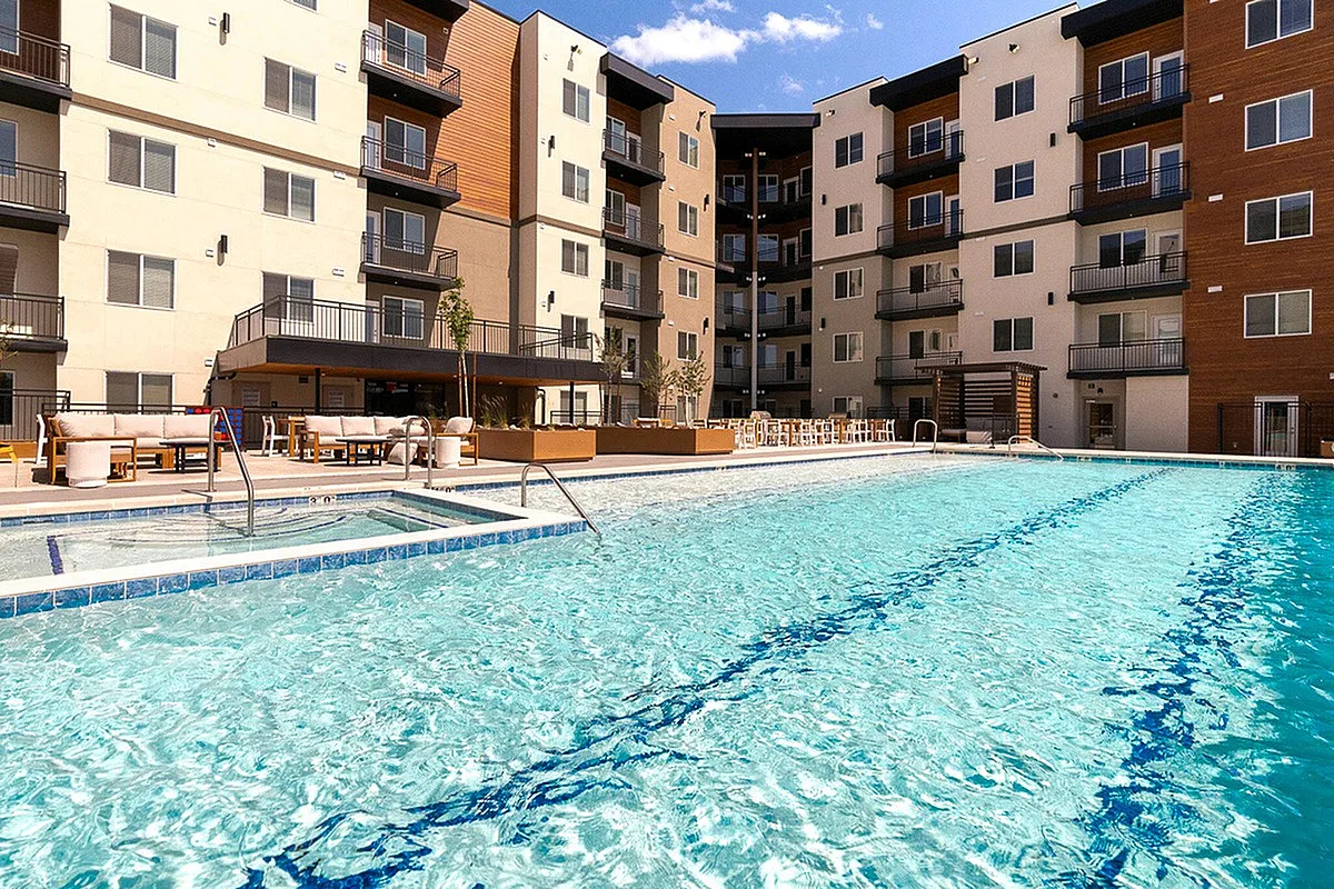 Current Apartments' outdoor pool, with modern balconies and stylish lounge areas under a blue sky.
