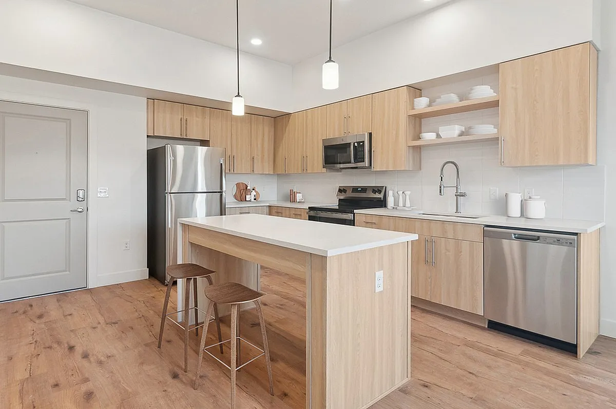 Sleek modern kitchen at Current Apartments in SLC with light wood cabinetry, stainless steel appliances, and a stylish island with seating, perfect for entertaining.