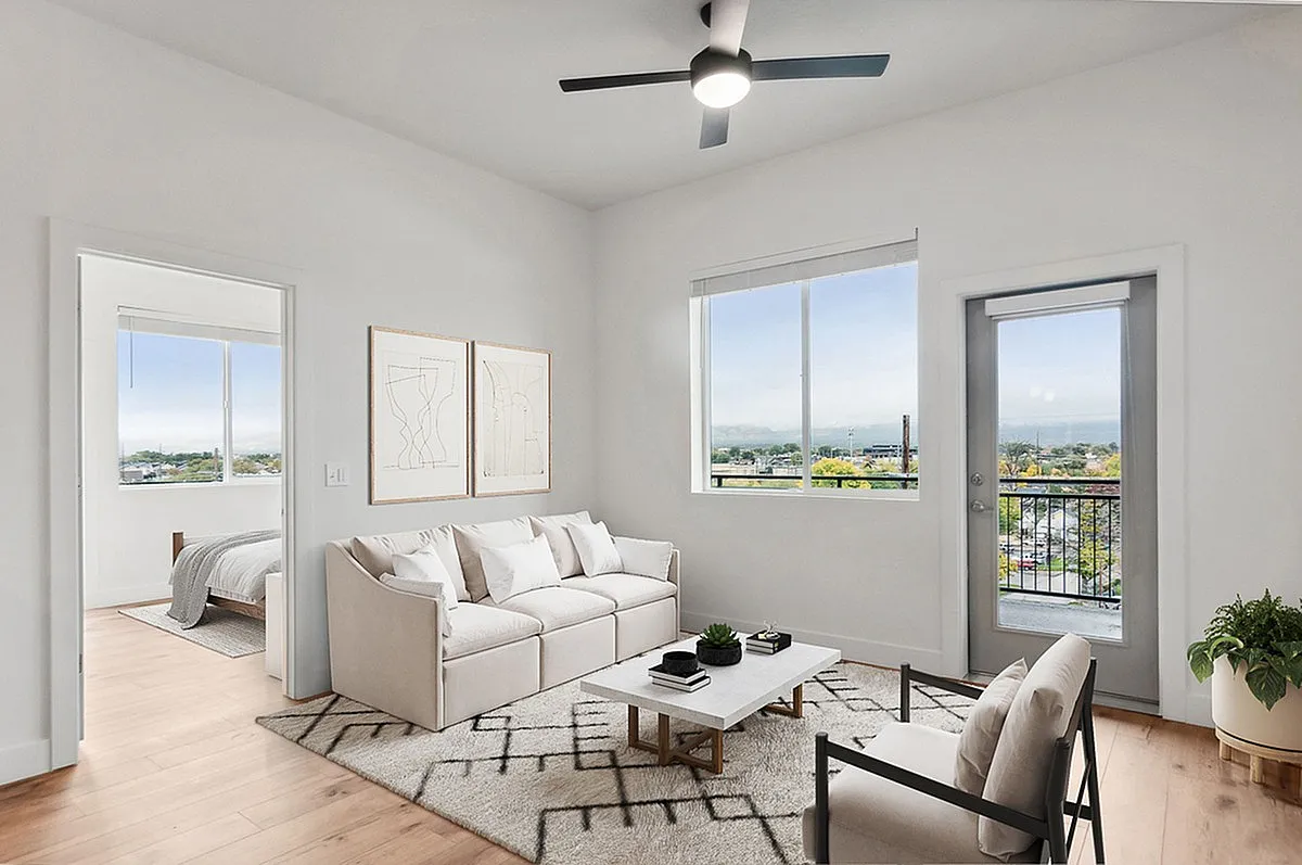 Bright and modern living room with elegant white sofa, geometric rug, and large windows offering stunning views of Salt Lake City at Current Apartments..