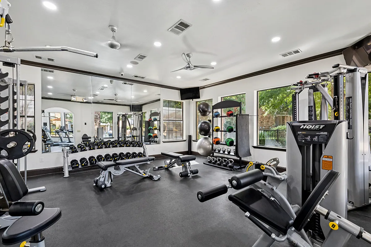Modern fitness center with advanced gym equipment, free weights, and natural light streaming through large windows at Enclave on Golden Triangle Apartments in Fort Worth Texas