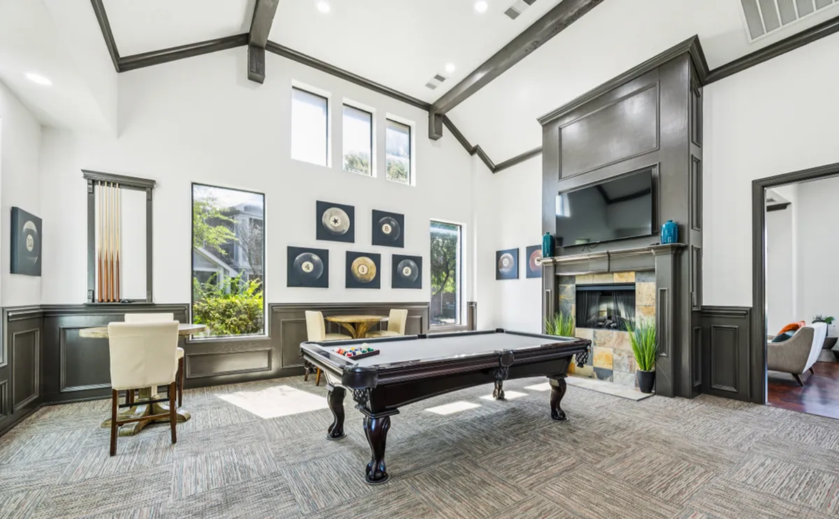 Luxurious game room featuring a sleek pool table, elegant seating area, and a cozy fireplace under high ceilings at Enclave on Golden Triangle Apartments in Fort Worth Texas