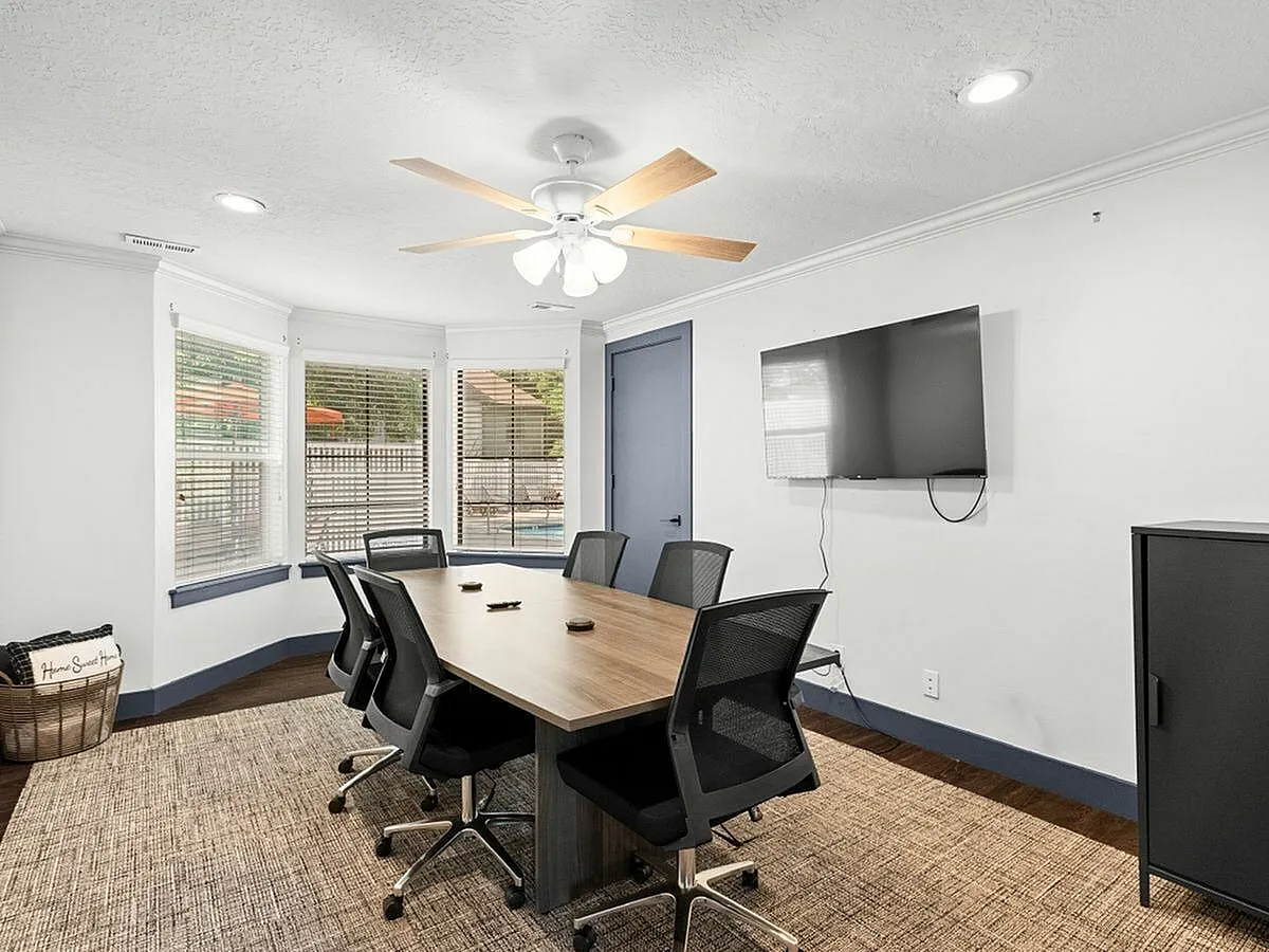 Contemporary conference room featuring a large wooden table, sleek office chairs, and a wall-mounted TV, with ample natural light from bay windows  at Apt CoWork at Cottonwood Apartments in SLC