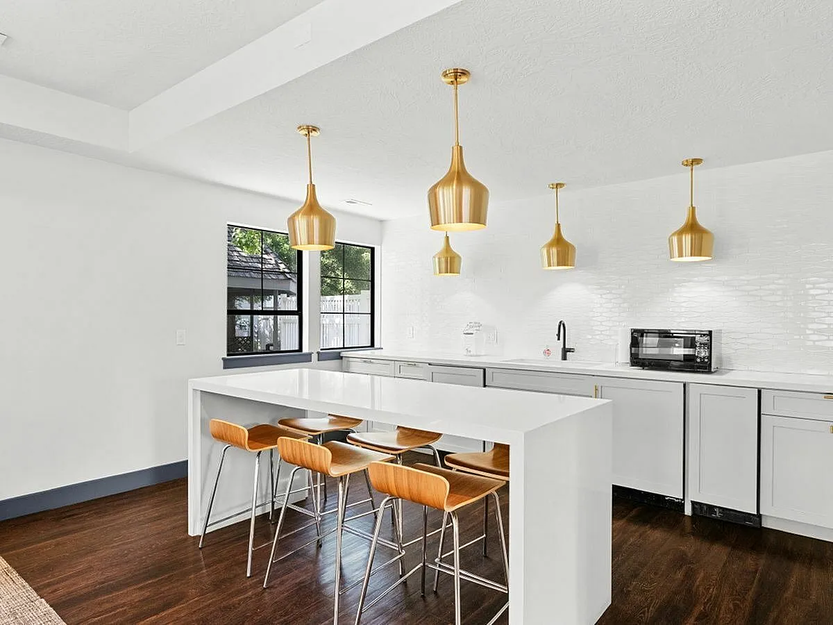 Chic modern kitchen with sleek white cabinetry, elegant gold pendant lights, and a stylish island with wooden stools  at Apt CoWork at Cottonwood Apartments in Salt Lake City