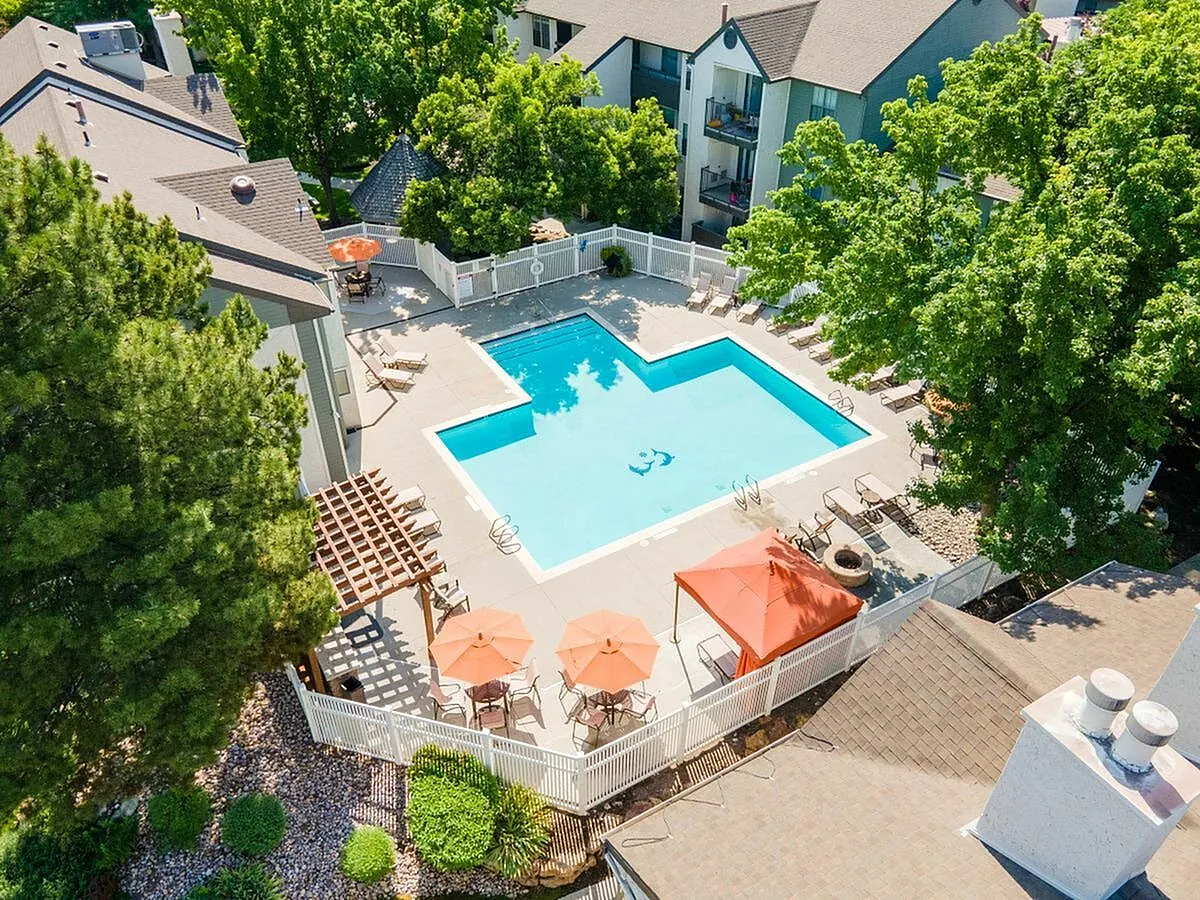 Inviting aerial view of a modern apartment complex with a large pool, surrounded by lush greenery and sunlit relaxation areas at Cottonwood Apartments in SLC