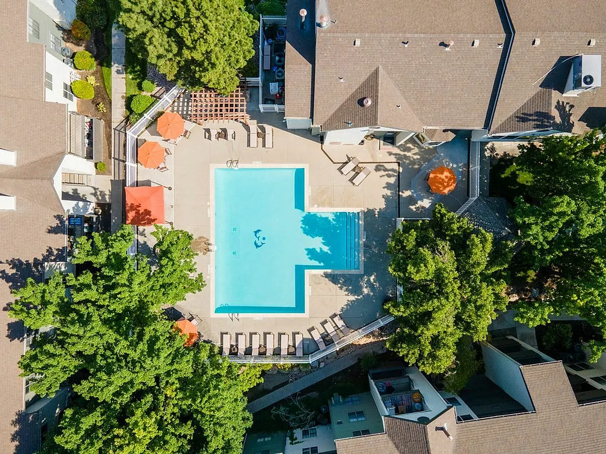Aerial view of a luxury apartment complex featuring a sparkling swimming pool surrounded by lush greenery and sun loungers, offering a perfect oasis for relaxation at Cottonwood Apartments in Salt Lake City