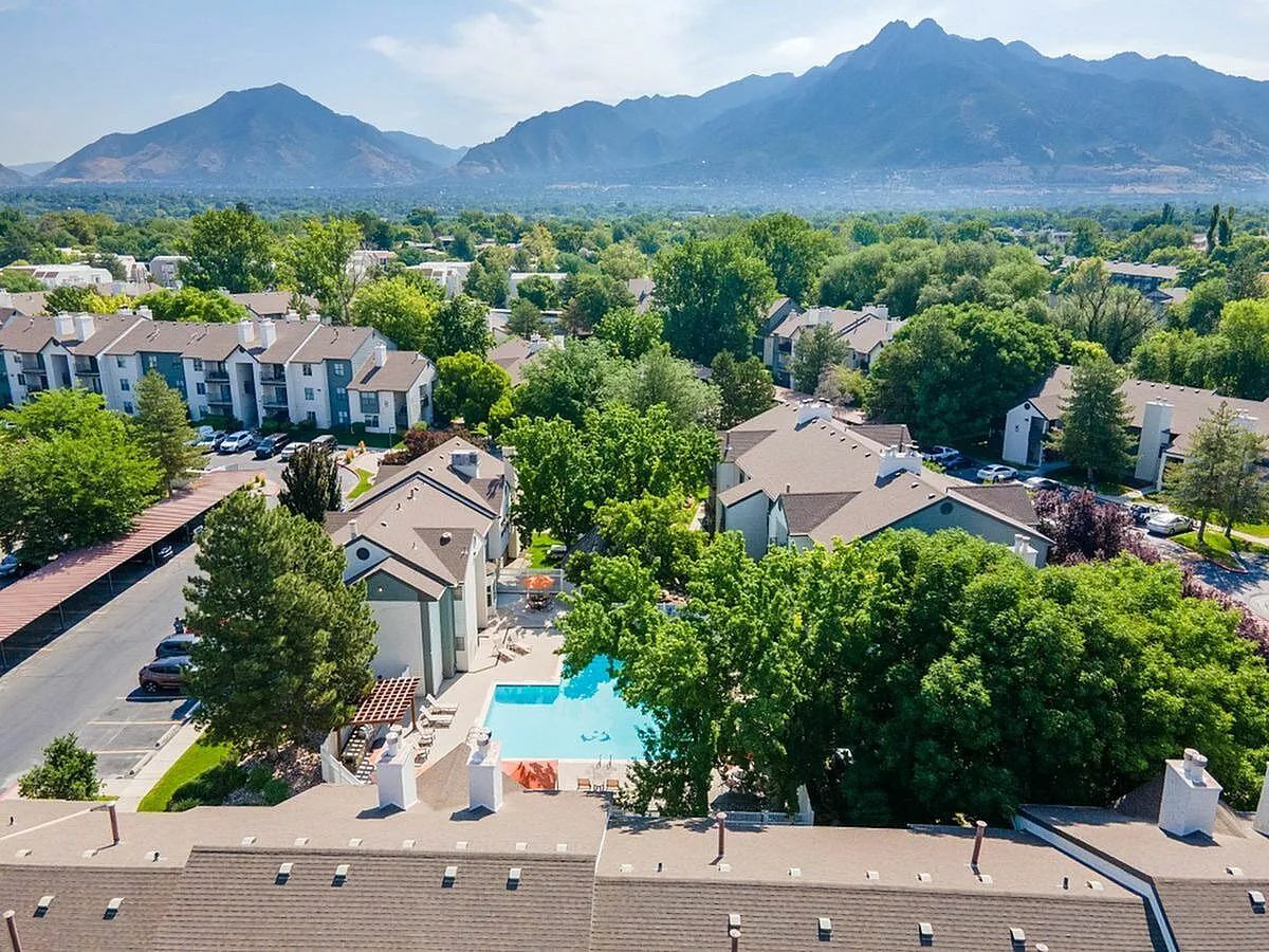 Stunning aerial view of a serene residential community with a sparkling swimming pool, surrounded by lush greenery and majestic mountain backdrop at Cottonwood Apartments in SLC