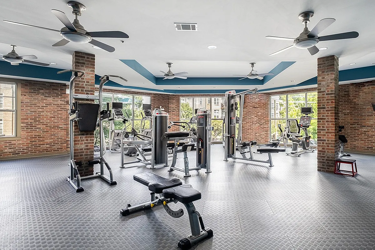 Modern fitness center at Alpha Mill with state-of-the-art gym equipment, featuring large windows, brick accents, and an open, airy layout.