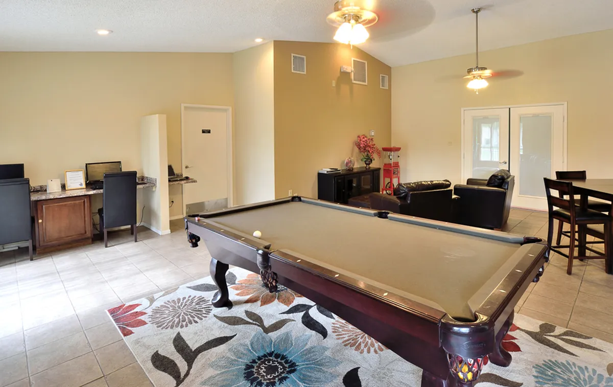 Chic recreational room at Camelot Apartments featuring a sleek pool table, comfortable seating area, and modern workspace, perfect for entertainment and productivity.