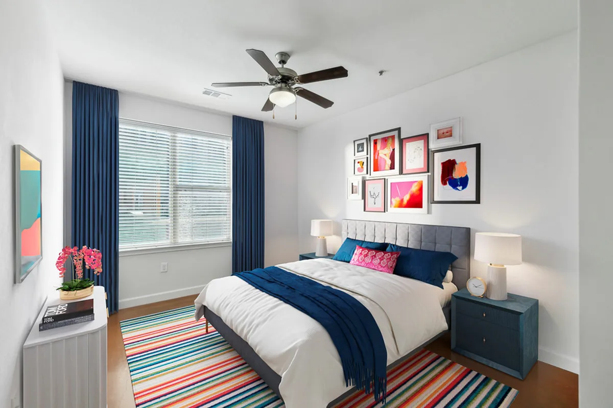 Elegant bedroom at The Melrose showcasing modern art gallery wall, vibrant striped rug, and plush bedding in a cozy, light-filled space.