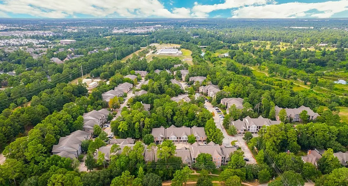 Scenic aerial view of a lush, green residential community surrounded by trees, featuring modern houses with spacious yards and a bright blue sky above  at Raveneaux Apartments in Houston Texas