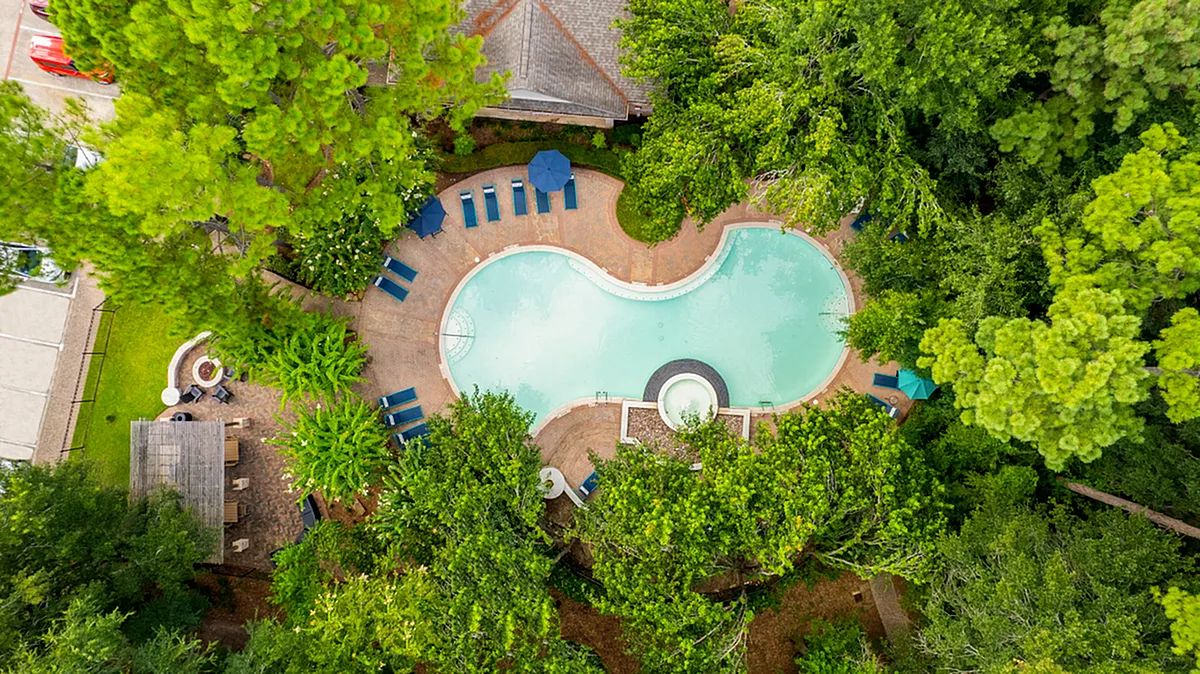 Lush aerial view of a resort-style swimming pool surrounded by vibrant greenery and luxurious loungers, offering a serene escape at Raveneaux Apartments in Houston Texas