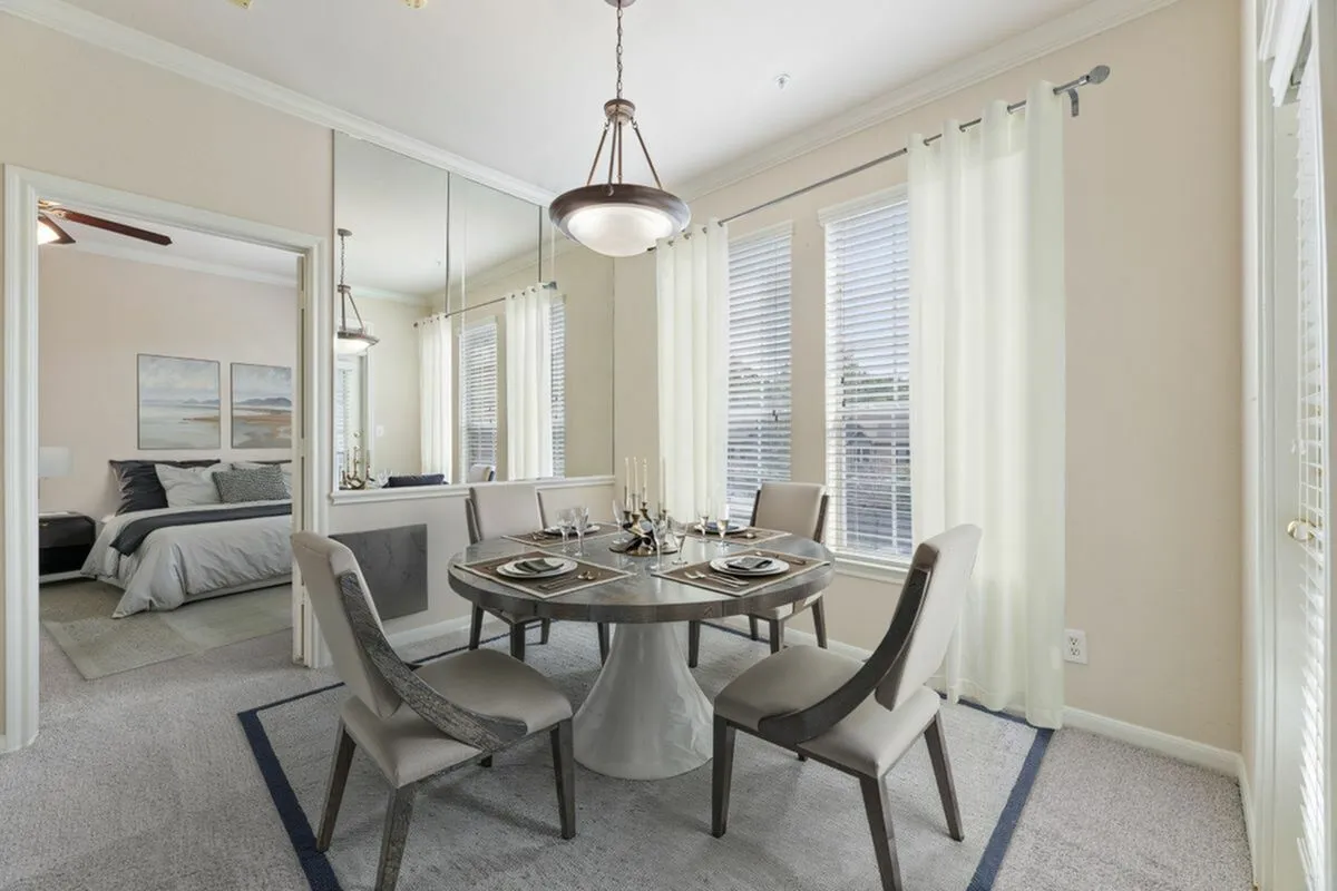 Elegant dining area with a contemporary round table, stylish chairs, and large windows offering natural light, adjacent to a cozy bedroom at Raveneaux Apartments in Houston