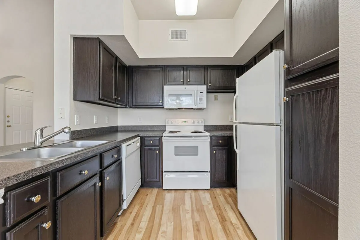 Modern kitchen with elegant dark wood cabinets, spacious countertops, and essential white appliances on sleek hardwood flooring at Raveneaux Apartments in Houston TX