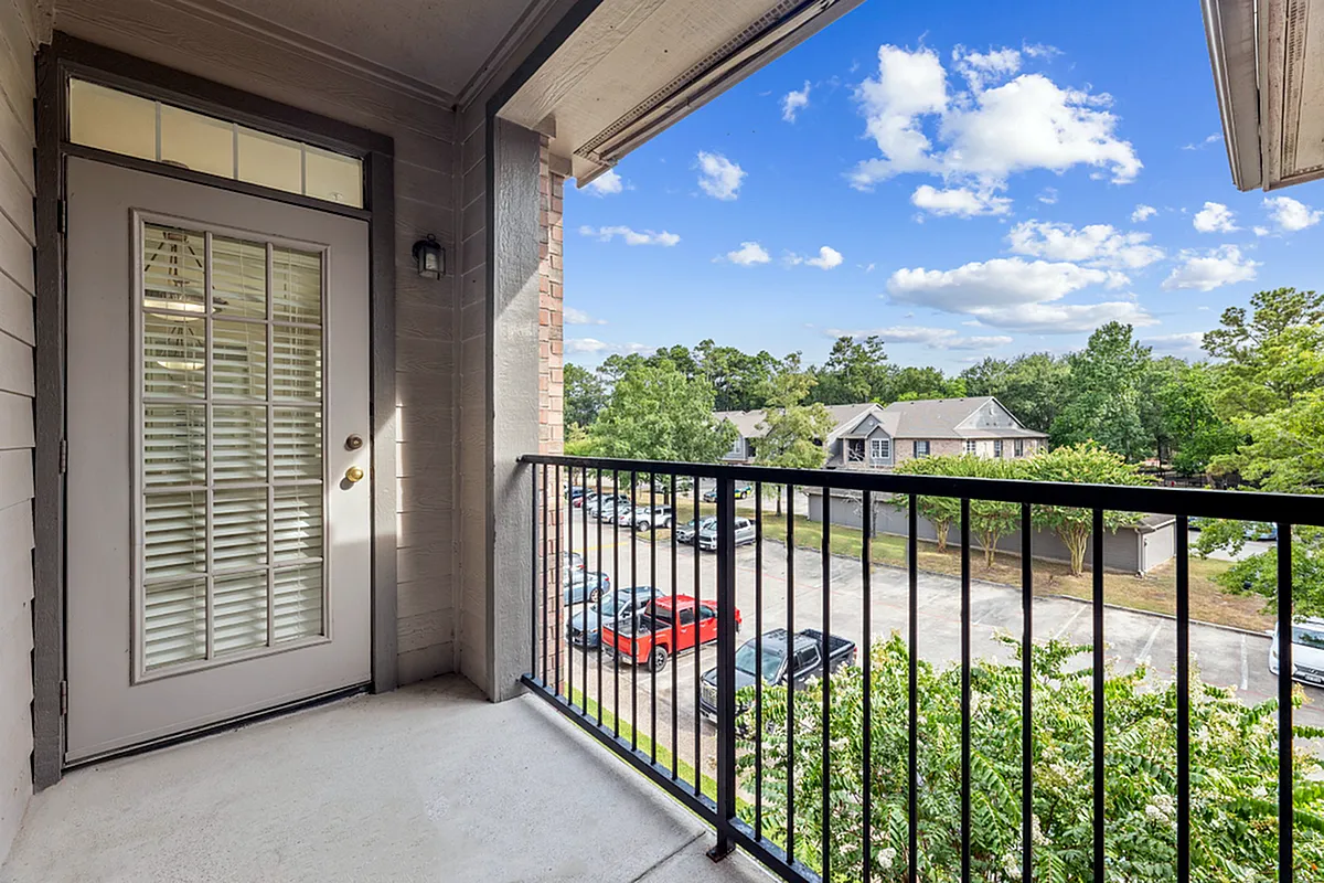 Charming balcony offering a picturesque view of lush greenery and a peaceful neighborhood street, enhanced by a bright, clear sk yat Raveneaux Apartments in Houston