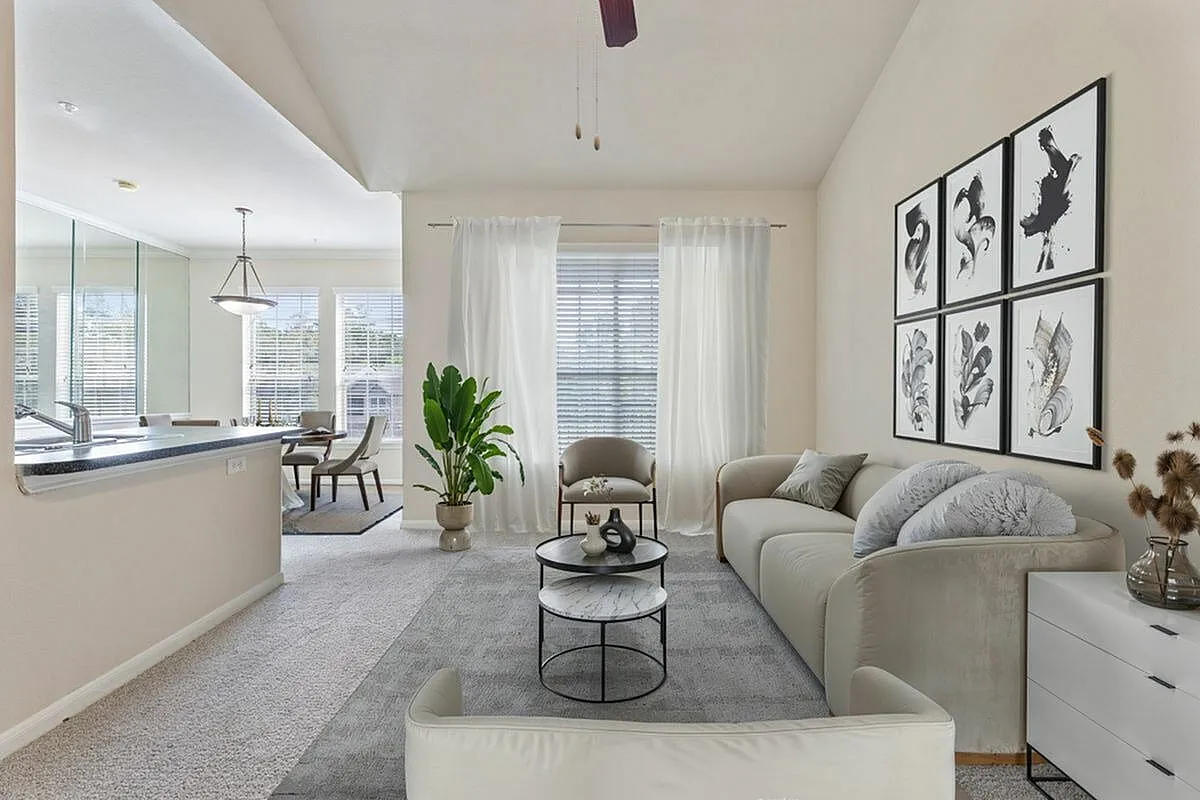 Bright and airy living room with modern decor, featuring a comfortable sofa, stylish wall art, and lush greenery, seamlessly connected to a well-lit dining area at Raveneaux Apartments in Houston