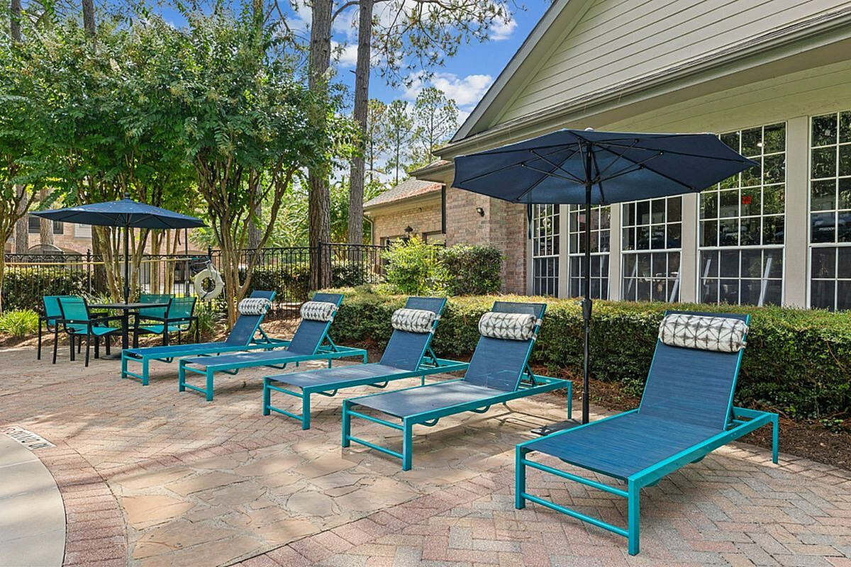 Charming outdoor area with cozy lounge chairs and umbrellas, perfect for relaxation amid lush greenery at Raveneaux Apartments in Houston TX