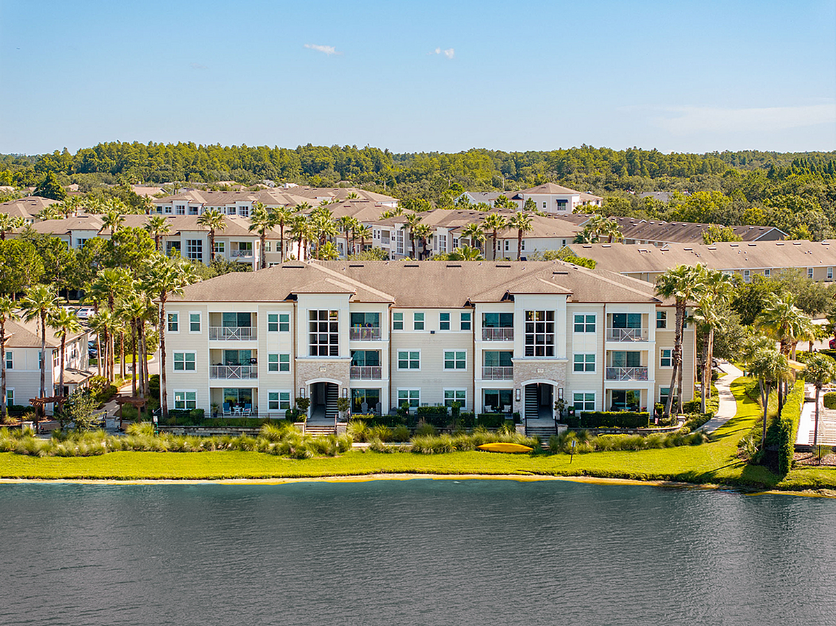 Charming lakeside apartment complex with palm trees and lush greenery, offering serene views and elegant architecture at the Marq Highland Park in Westchase