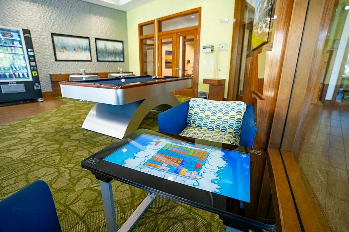 Luxurious recreation room featuring a modern pool table, vibrant lounge chairs, and an interactive gaming table, perfect for relaxation and entertainment at Apt CoWork at The Marq Highland Park in Westchase FL