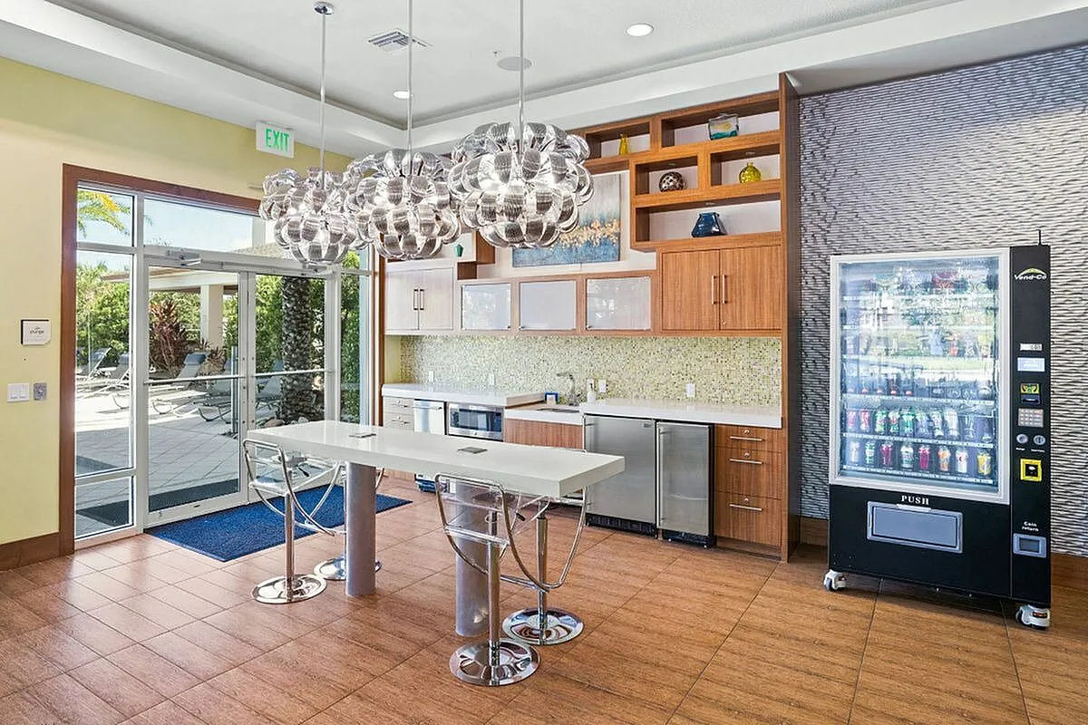 Coworking space with kitchen and snack station with elegant pendant lighting, sleek countertops, and a convenient vending machine, opening to a sunny outdoor patio at the Marq Highland Park Apt CoWork in Westchase Tampa