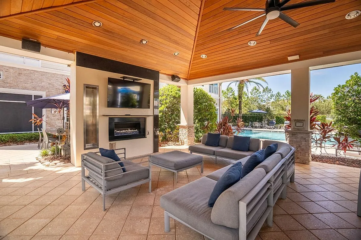 Luxurious outdoor lounge with elegant seating, modern TV setup, and view of a sparkling pool surrounded by lush greenery at The Marq Highland Park Apartments