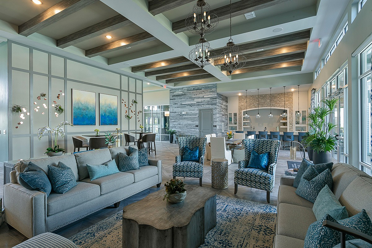 Luxurious open-concept clubroom at Cottonwood Clermont Apartments with elegant seating, vibrant artwork, and a stylish kitchen bar area, highlighted by modern chandeliers and natural light.