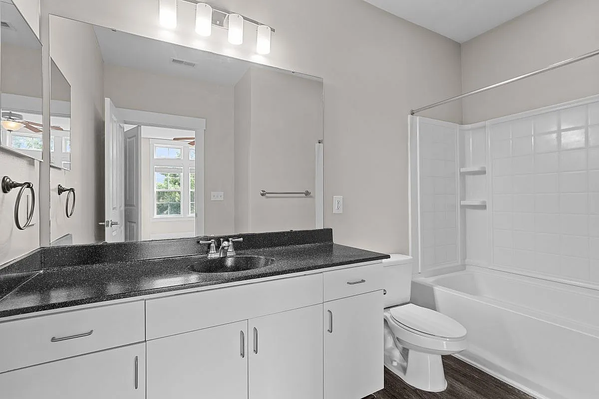 Bright and modern bathroom boasting elegant black countertops, sleek white cabinetry, and a large mirror for a spacious feel Garden Style Bedroom at Alpha Mill Apartments in NODA Charlotte