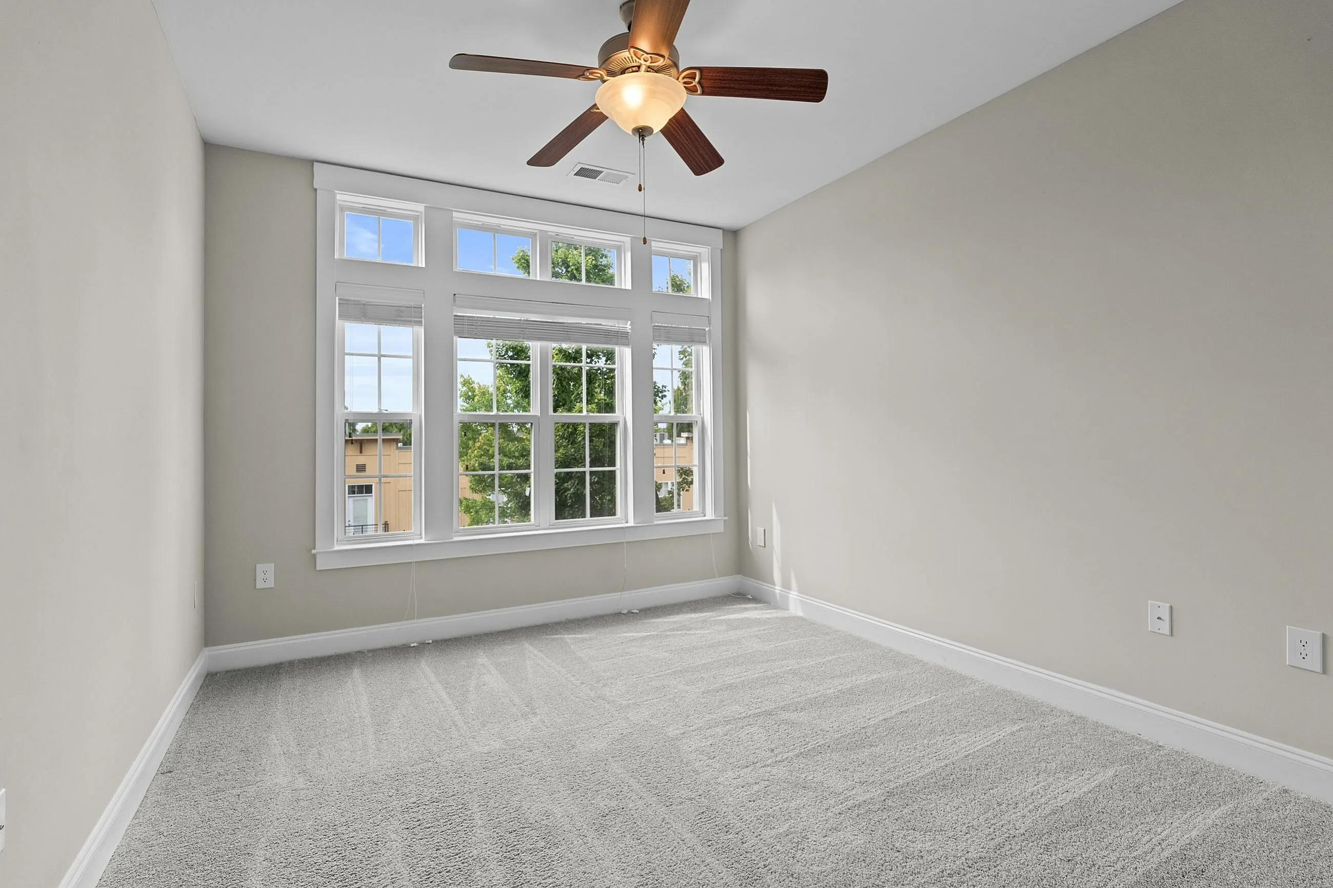 Bright and airy bedroom featuring large windows, plush carpet, and a ceiling fan Garden Style Bedroom at Alpha Mill Apartments in NODA Charlotte.