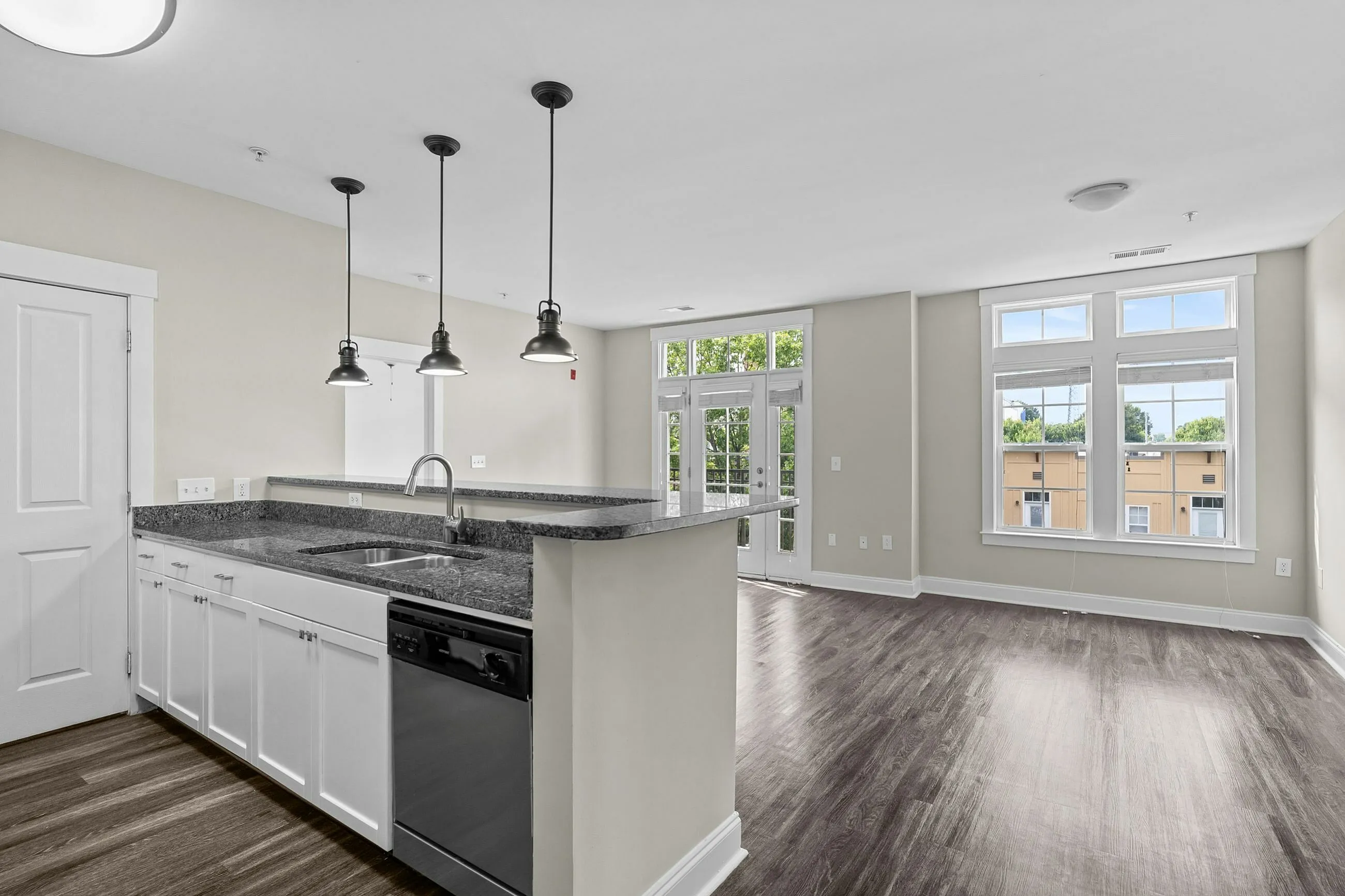 Bright and modern open-concept living space featuring a gourmet kitchen with sleek granite countertops, elegant pendant lighting, and expansive windows offering natural light and scenic views Garden Style Bedroom at Alpha Mill Apartments in NODA Charlotte.