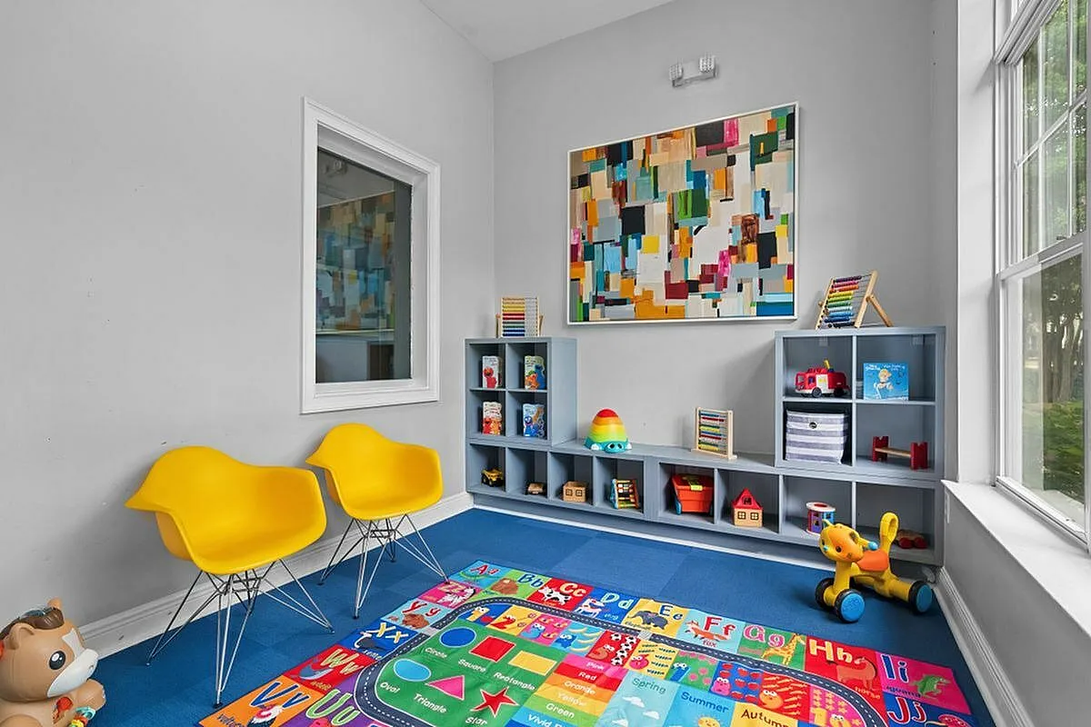 Bright and inviting playroom featuring vibrant educational decor, modern yellow chairs, and ample storage for toys and books at Cottonwood Reserve in Charlotte, NC