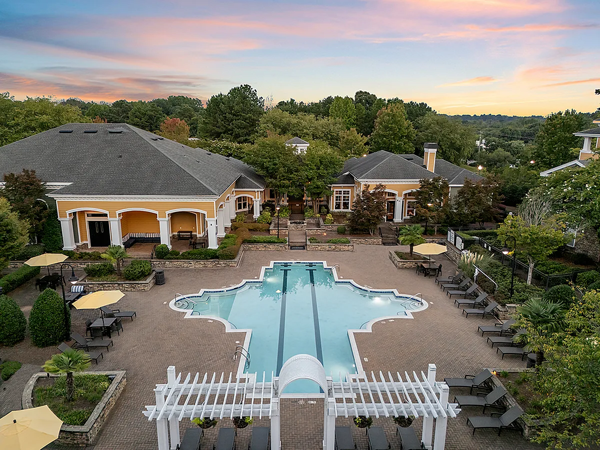 Elegant apartment complex with luxurious pool area, surrounded by lush greenery and charming architecture under a picturesque sunset sky at Cottonwood Reserve in Charlotte, NC