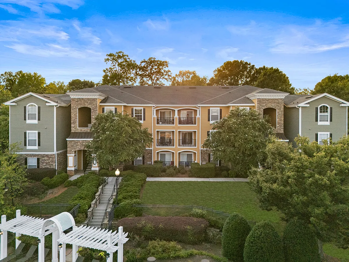 Charming apartment complex with elegant architectural features, lush greenery, and inviting pathways under a bright blue sky at Cottonwood Reserve Apartments in Charlotte, NC