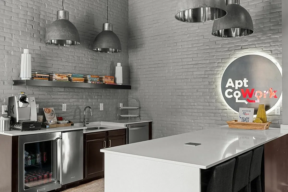 Modern coworking kitchen with sleek countertops, industrial lighting, and stocked coffee station at Apt CoWork.