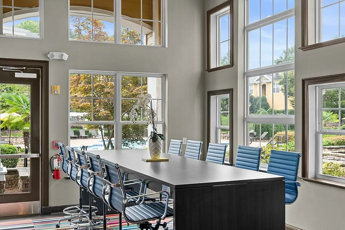 Elegant conference room with floor-to-ceiling windows offering lush outdoor views, featuring modern blue swivel chairs and a sleek dark table at Apt CoWork in Charlotte, NC