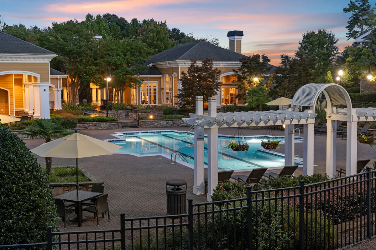 Elegant apartment complex with resort-style pool area, surrounded by lush greenery and beautifully lit architecture at sunset at Cottonwood Reserve Apartments in Charlotte NC