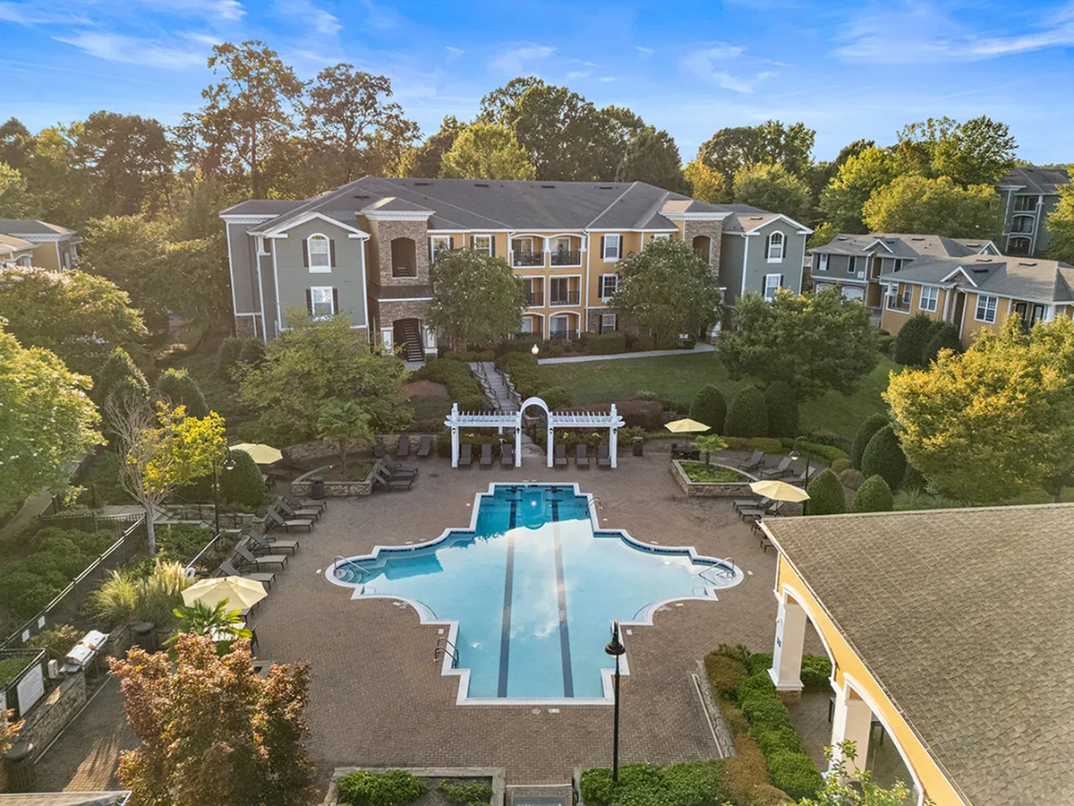 Charming apartment complex with elegant architecture, lush greenery, and a stunning pool area under a clear blue sky at Cottonwood Reserve Apartments in Steele Creek Charlotte NC