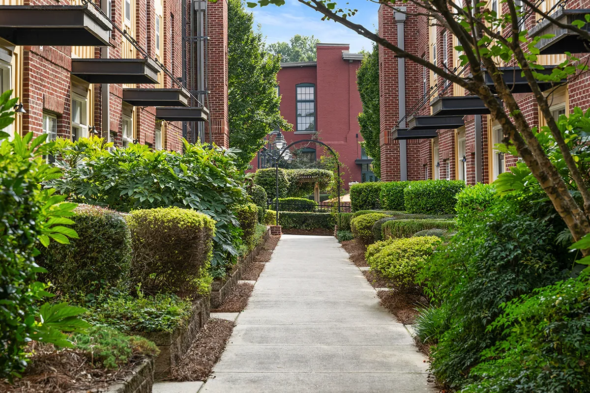 Charming outdoor pathway lined with lush greenery and elegant brick buildings, creating a serene and inviting ambiance at Alpha Mill Apartments in Uptown Charlotte NC
