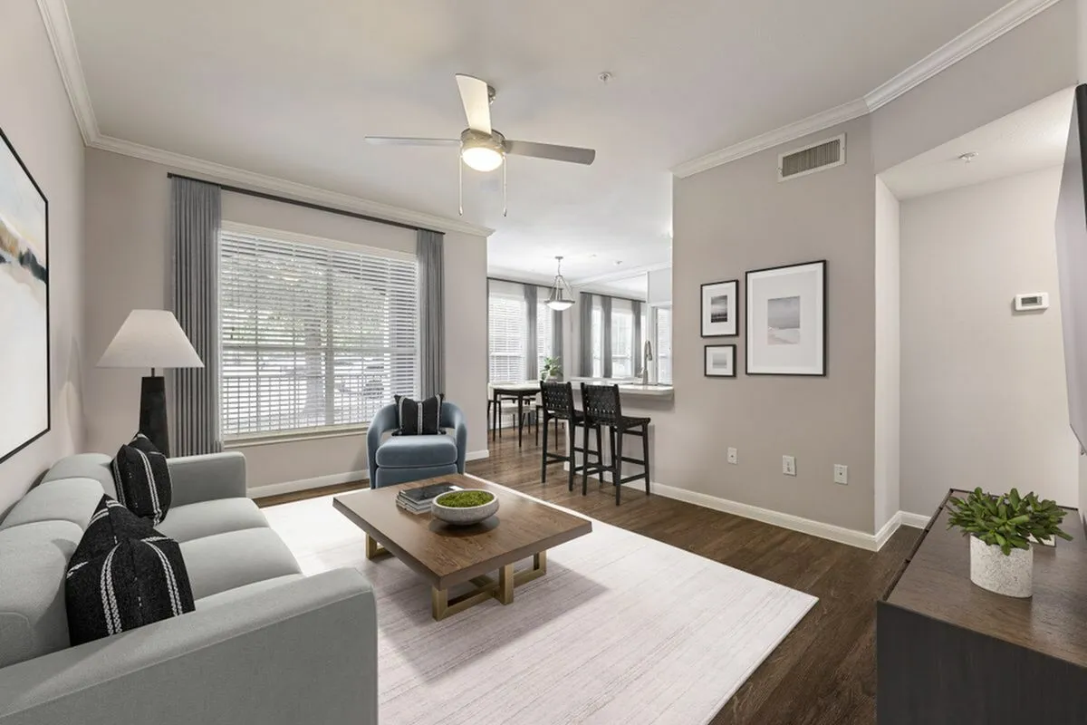 Chic living room with modern decor, featuring a cozy sofa, elegant coffee table, and a bright open-plan layout leading to a stylish kitchen and dining area at Raveneaux Apartments in Houston, Texas.